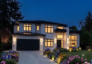 Une maison moderne à deux étages, dotée d’un garage, de grandes fenêtres et d’un éclairage extérieur soigné.