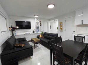 Un salon moderne avec un canapé noir, une table à manger et un téléviseur à écran plat fixé au mur.