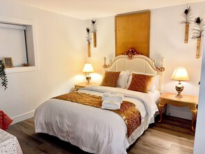 Un lit bien fait, recouvert d’une couvre-lit blanche et dorée, avec deux lampes de chevet et un grand miroir accroché au mur.