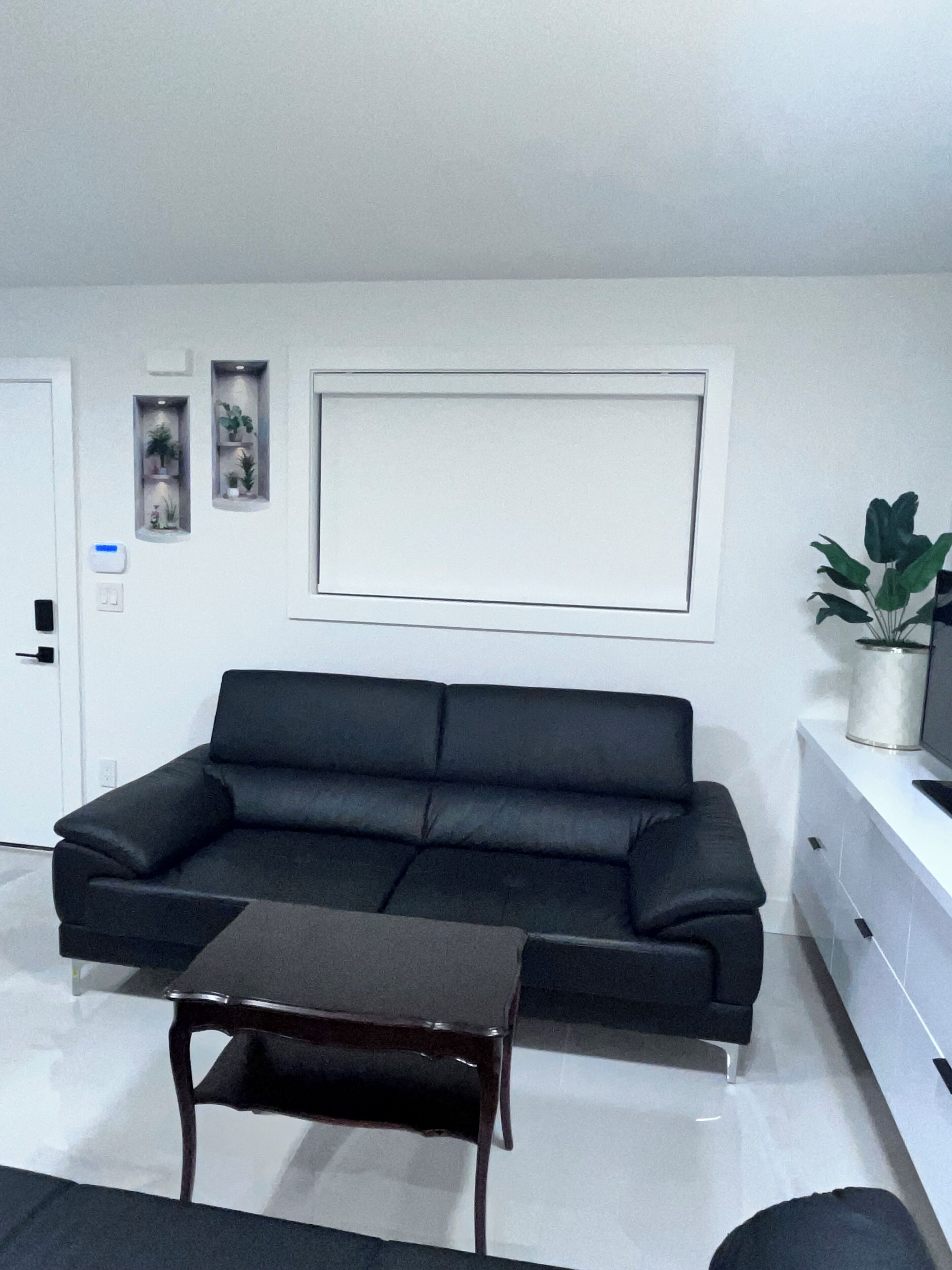 A modern living room with a black leather sofa, a wooden coffee table, and a white cabinet.