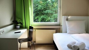 Habitación de hotel con cama, escritorio, silla, ventana y vistas a árboles, además de un radiador.