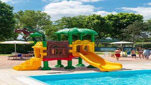 Une aire de jeux avec un toboggan et des structures d’escalade, située près d’une piscine.