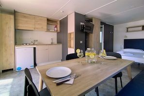A compact hotel room with a kitchenette, a dining table set with plates, cutlery, and a glass of wine, and a bed with a dark headboard. - Cozy mobile home in Cesenatico (Cesenatico)