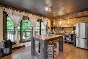 Una cocina rústica con armarios de madera, una mesa grande de madera y un refrigerador.