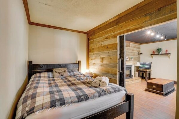Un dormitorio con techo de madera, una cama con colcha escocesa, una mesita de noche y un televisor en una esquina.