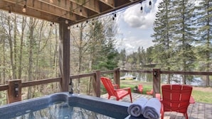 Ein Whirlpool auf einer Holzterrasse mit Blick auf einen Wald und einen See.