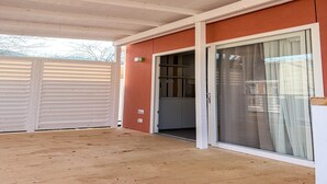 Een overdekt terras met houten vloer, een schuifdeur en een raam met witte kozijnen.