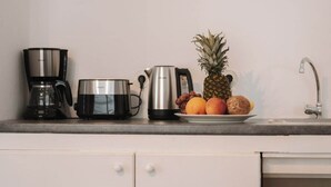 Uma bancada de cozinha com cafeteira, xícara, chaleira e um prato de frutas.