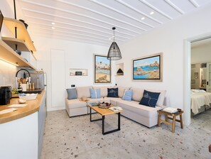 A modern living room with a sofa, coffee table, and a kitchen area with a sink and counter. - Apaggio Boutique House (Andros)