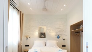Una habitación de hotel con una cama grande, un armario de madera, un aire acondicionado instalado en la pared y una mesita con una lámpara.