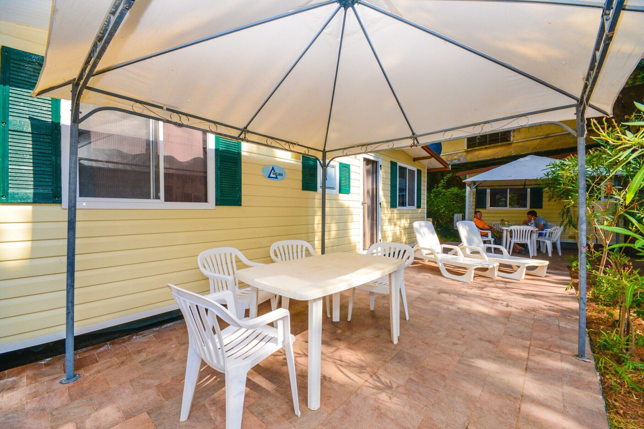Une terrasse extérieure avec une table et des chaises, protégée par un grand parasol, et entourée de verdure.