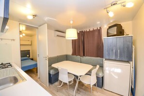 A compact kitchenette with a gas stove, a sink, a refrigerator, and a dining area with a table and chairs. - High-quality mobile home on Lake Garda (Toscolano - Maderno)