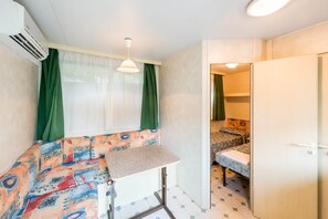 A compact room with a kitchenette, a bed with patterned bedding, a small table, and a door leading to another room. - High-quality mobile home on Lake Garda (Toscolano - Maderno)