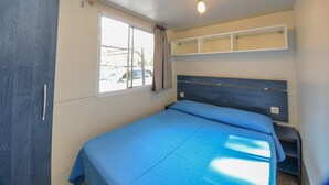 Een slaapkamer met een bed, een raam, een plafondlamp en een plank boven het bed.