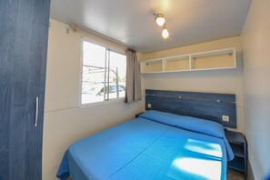Ein Schlafzimmer mit Bett, Fenster, Deckenleuchte und einem Regal über dem Bett.