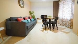 Een woonkamer met een bank, een eettafel met stoelen, een televisie en een decoratieve spiegel.