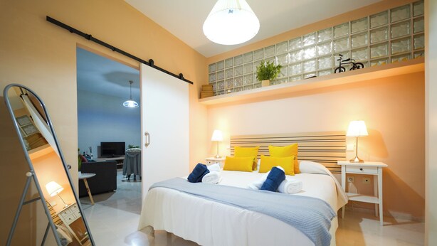 Een moderne slaapkamer met een groot bed, nachtlampjes en uitzicht op de woonruimte.