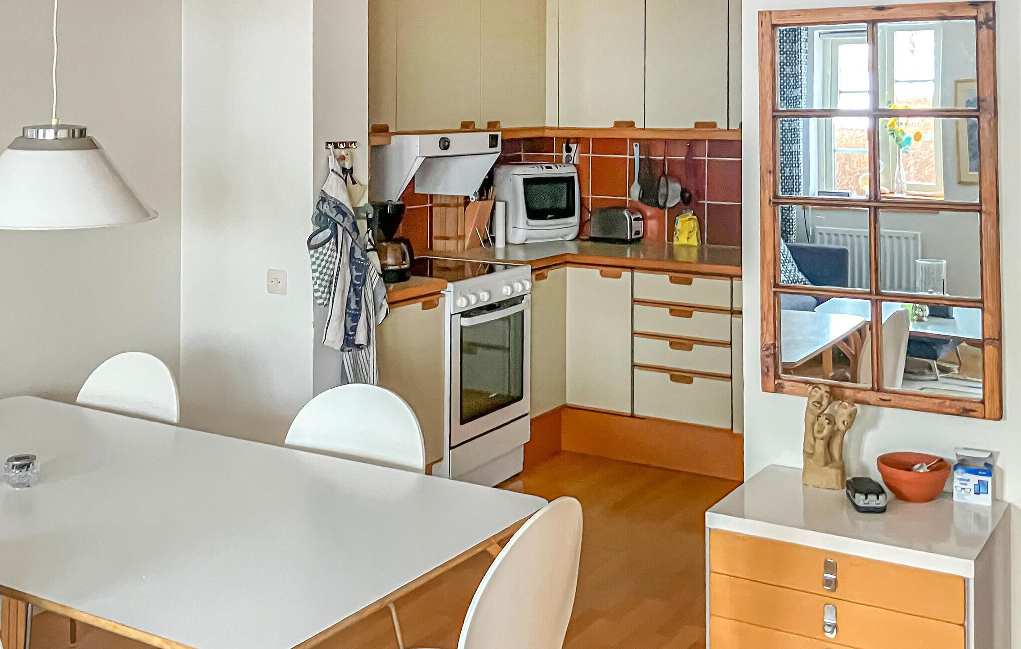 A compact kitchen with a stove, microwave, and wooden cabinets. There is a dining table with chairs and a window with a view of the outside.