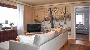 A living room with a sofa, a television, and a painting of a forest scene. - 4 bedroom beautiful home in Glemmingebro (Glemmingebro)