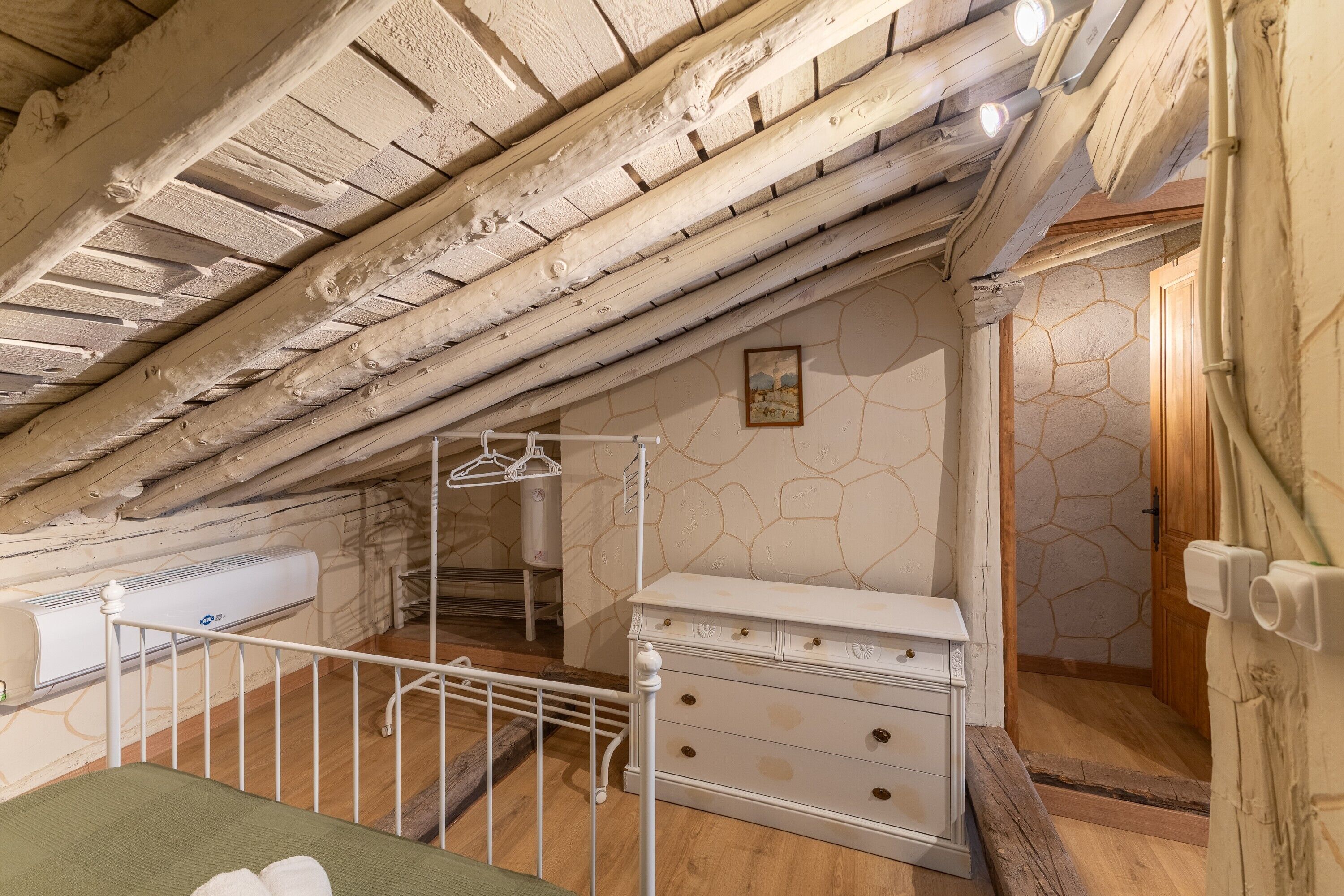 A room with a sloped ceiling, a radiator, a white dresser, and a hanging coat rack.