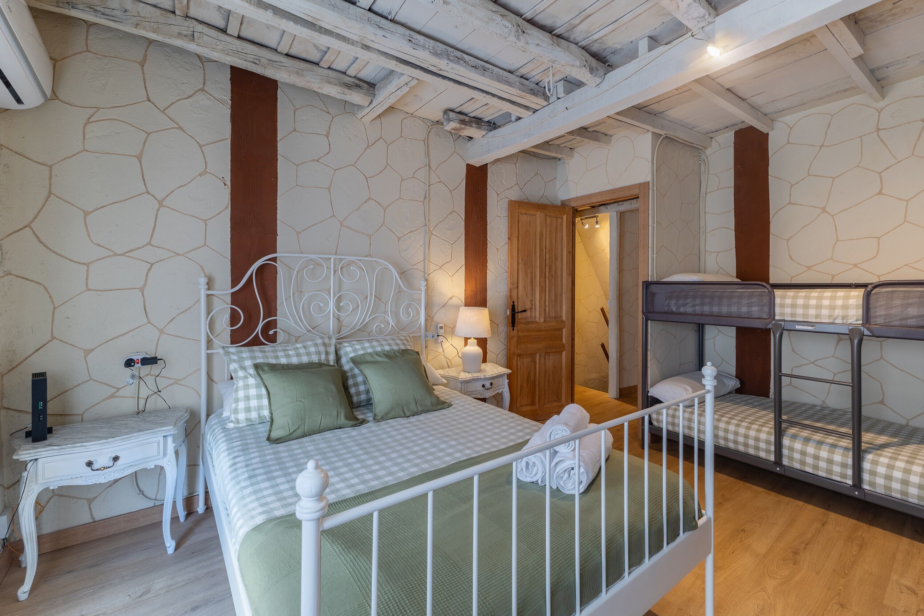 Un dormitorio con cama, mesita de noche, lámpara y literas.