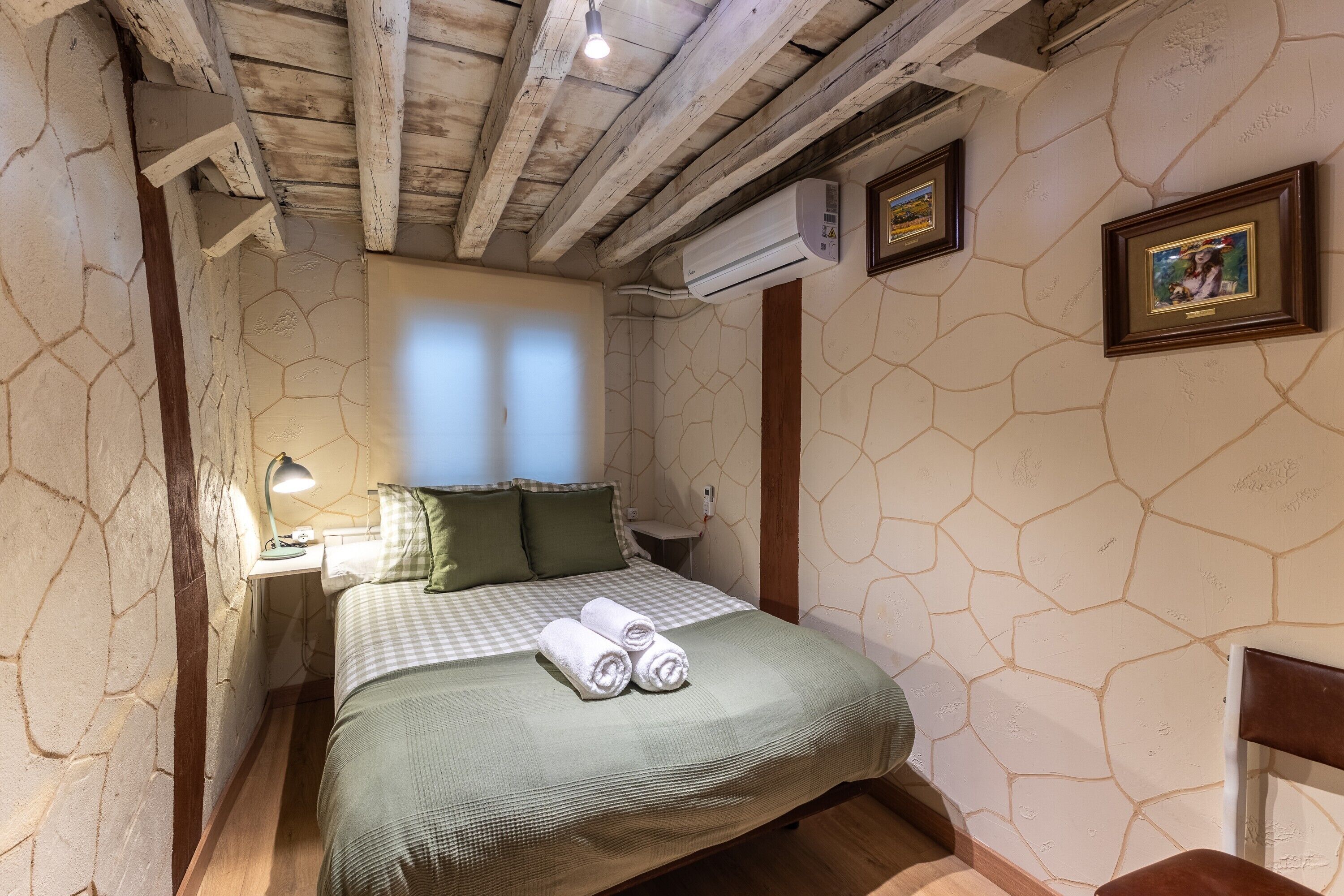 Een kamer met een bed, nachtkastje, wandairconditioner en een ingelijste foto.