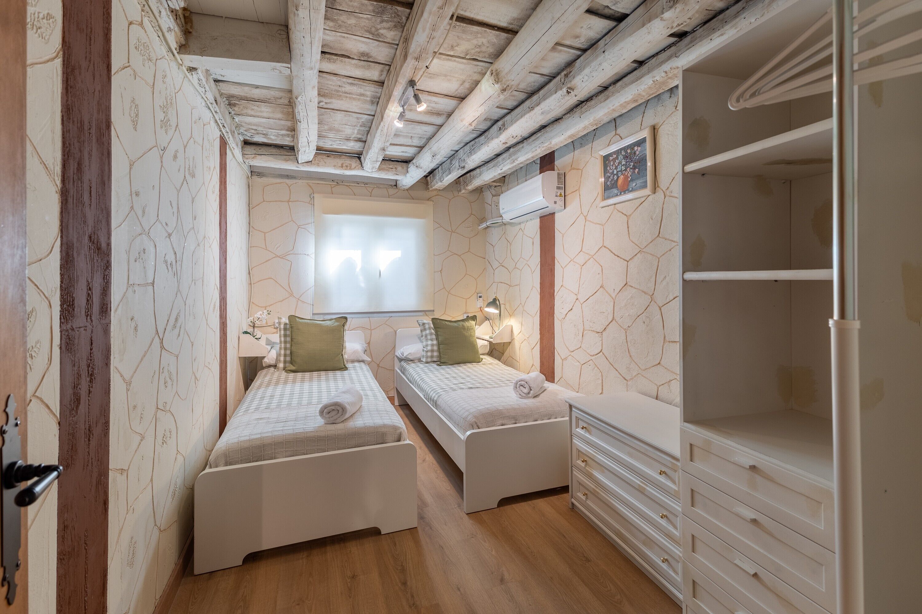 Una habitación con dos camas, techo de madera, ventana, armario y aire acondicionado instalado en la pared.