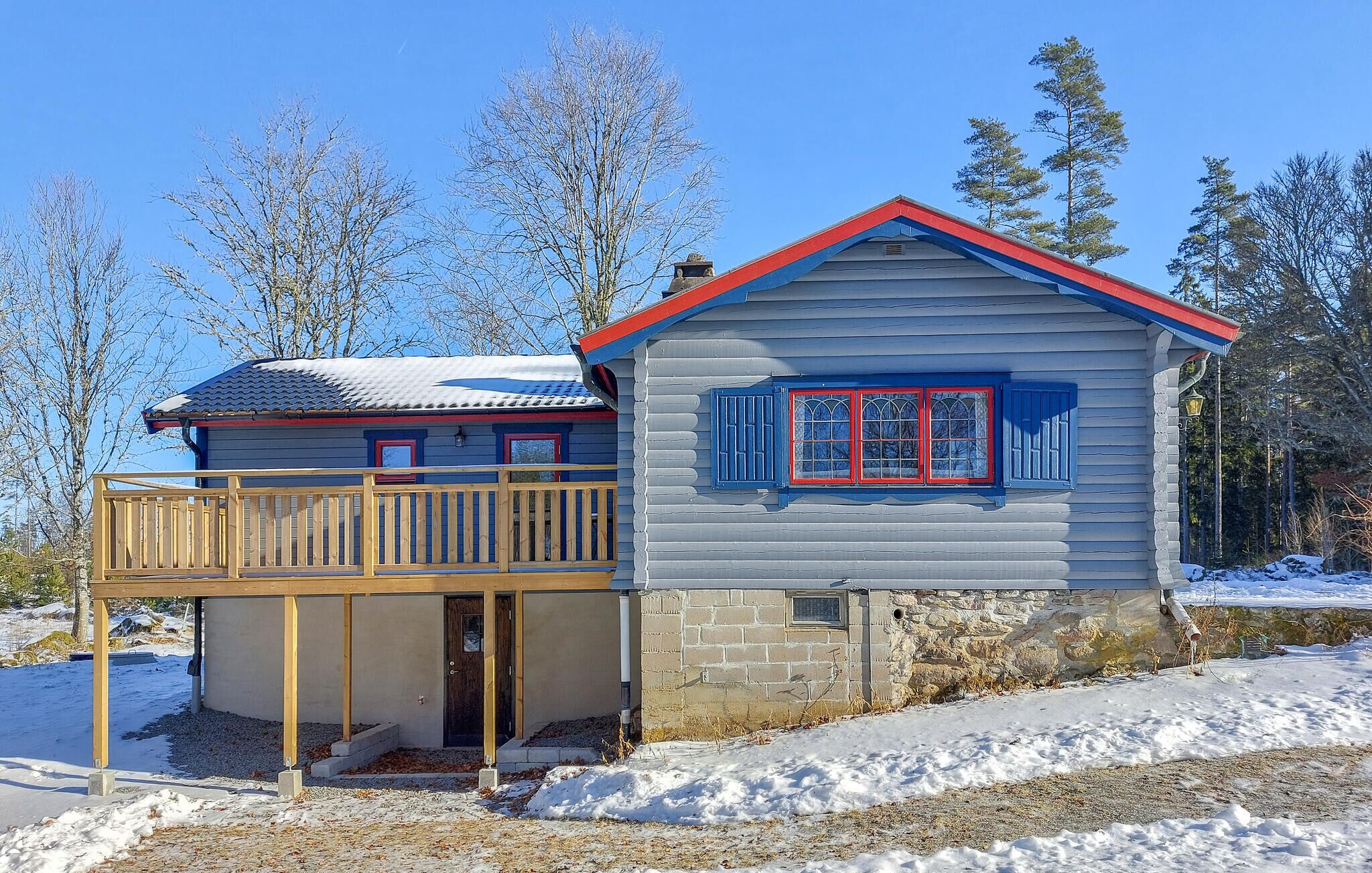 Eine Holzhütte mit Balkon und ein separates Gebäude mit rotem Dach und blauen Fensterläden.