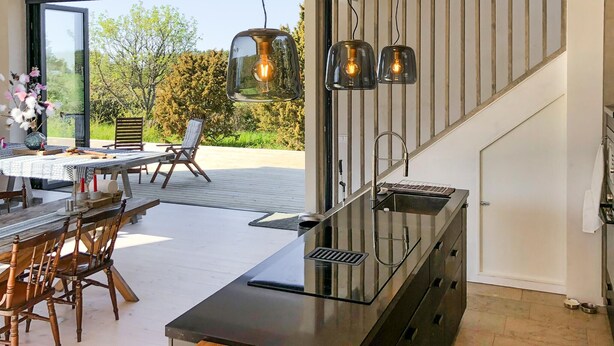 Una cocina moderna con estufa integrada, un comedor con sillas de madera y vistas al exterior.
