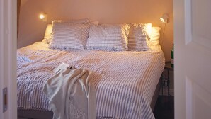 A neatly made bed with striped bedding and pillows, a bedside lamp, and a bottle of wine on a small table beside the bed. - Awesome apartment in Kyrkesund with WiFi (Kyrkesund)