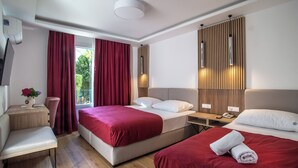Hotellihuone, jossa on kaksi sänkyä, työpöytä, tuoli ja ikkuna, jossa on punaiset verhot.