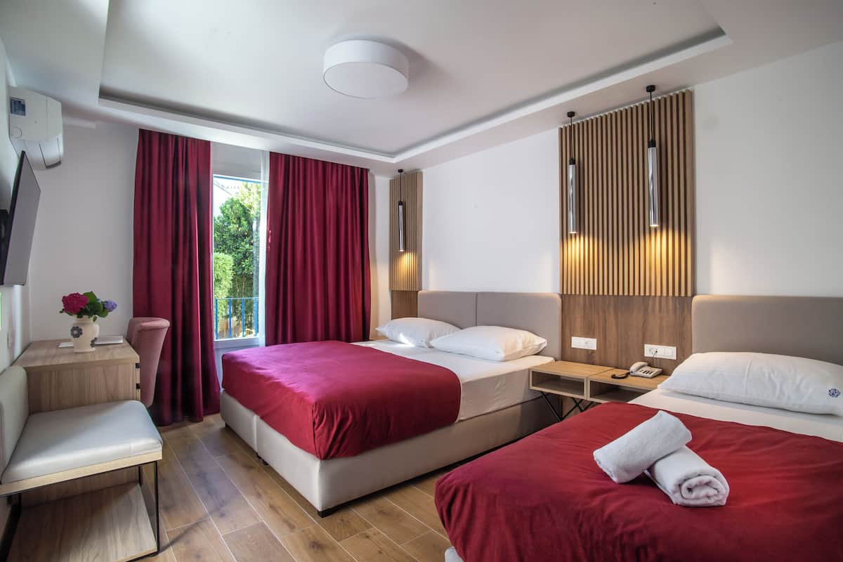 Hotellihuone, jossa on kaksi sänkyä, työpöytä, tuoli ja ikkuna, jossa on punaiset verhot.
