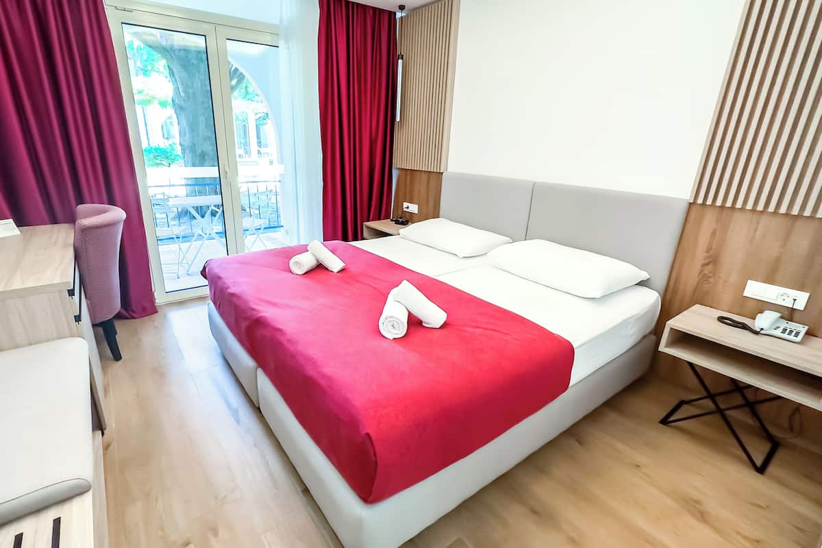 Hotellihuone, jossa on sänky, työpöytä, tuoli, pieni pöytä, puhelin ja ikkuna, jossa on verhot.