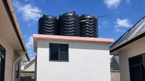 Ein Gebäude mit weißer Fassade, einem kleinen Fenster und drei schwarzen Wassertanks auf dem Dach.