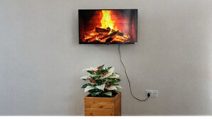 Ein an der Wand montierter Fernseher zeigt ein Bild eines Kaminfeuers und ist über eine Steckdose darunter mit Strom verbunden.