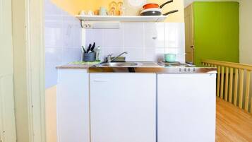 Eine kleine Küche mit weißen Schränken, einem Spülbecken und einer Arbeitsplatte. Eine grüne Wand und ein Holzboden sind zu sehen.