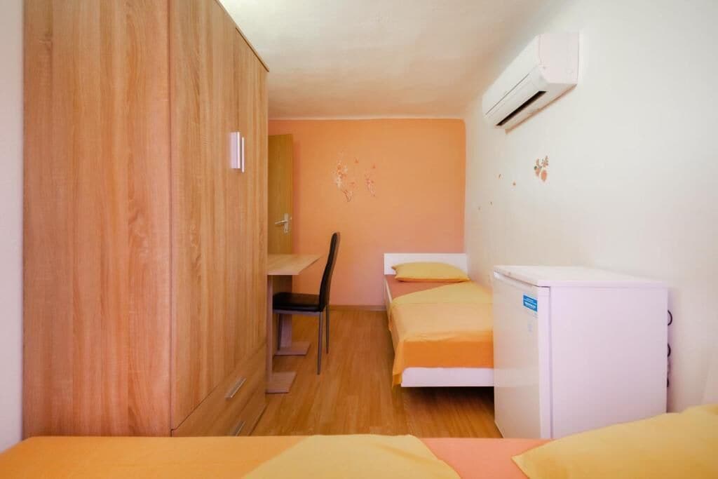Une petite pièce, de taille modeste, comprenant une armoire en bois, un bureau, deux lits et un réfrigérateur blanc.