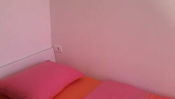 Een enkel bed met een roze kussen en oranje beddengoed in een kamer met roze wanden.