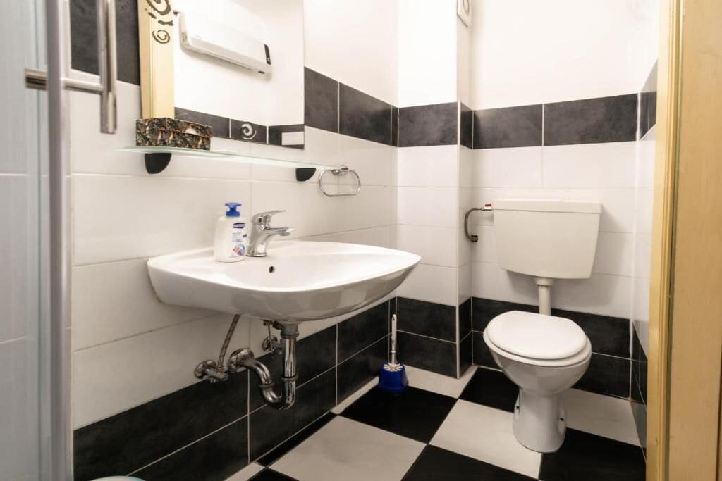 Une salle de bain avec un lavabo blanc, un carrelage noir et blanc et des toilettes blanches.