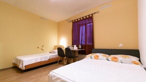 A hotel room with two single beds, a desk with a chair, and a window with purple curtains. - Hostel Martin (Koper)