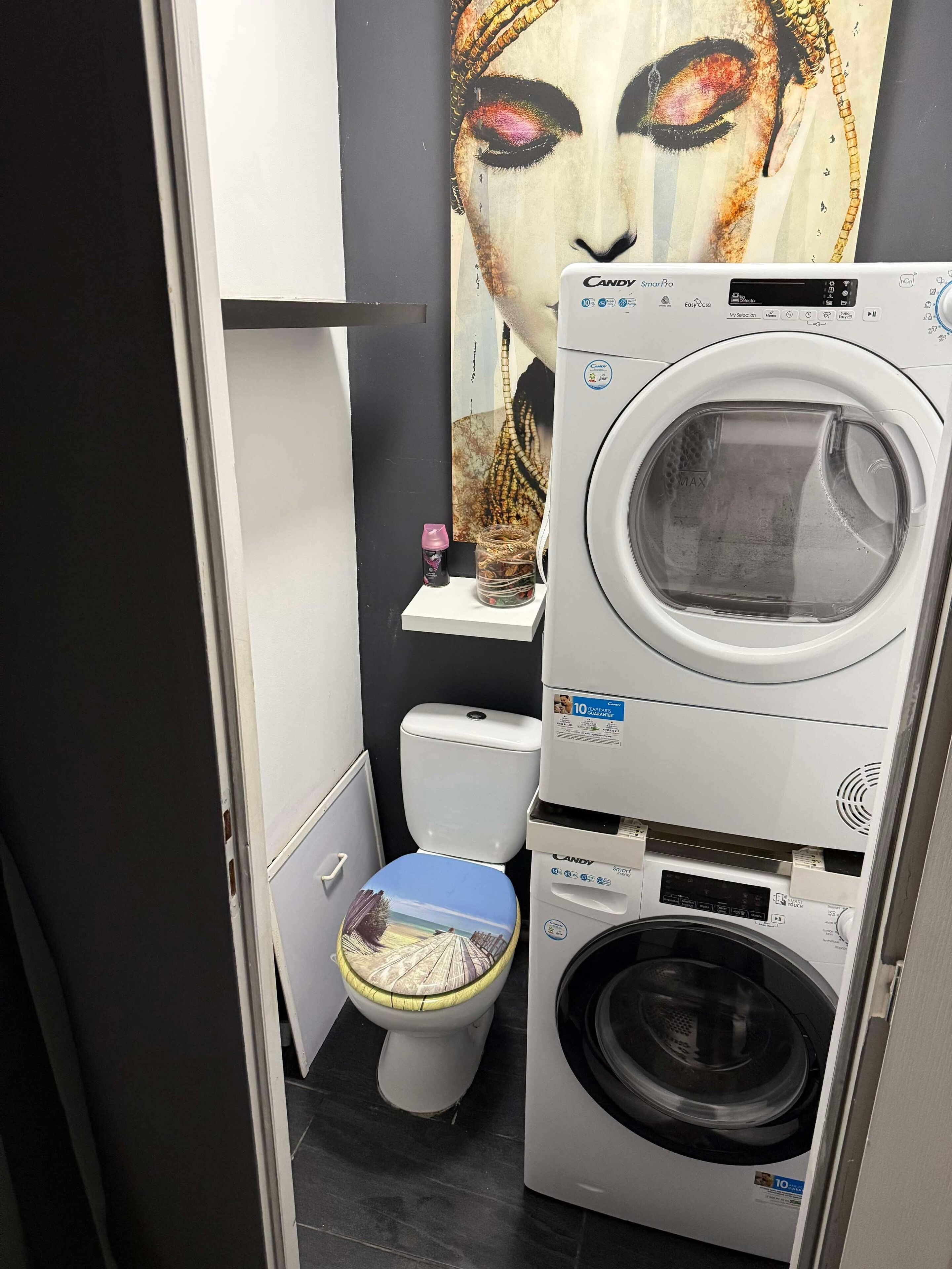 Ein kleines Badezimmer mit Toilette, Waschmaschine und einem großen Gemälde an der Wand.