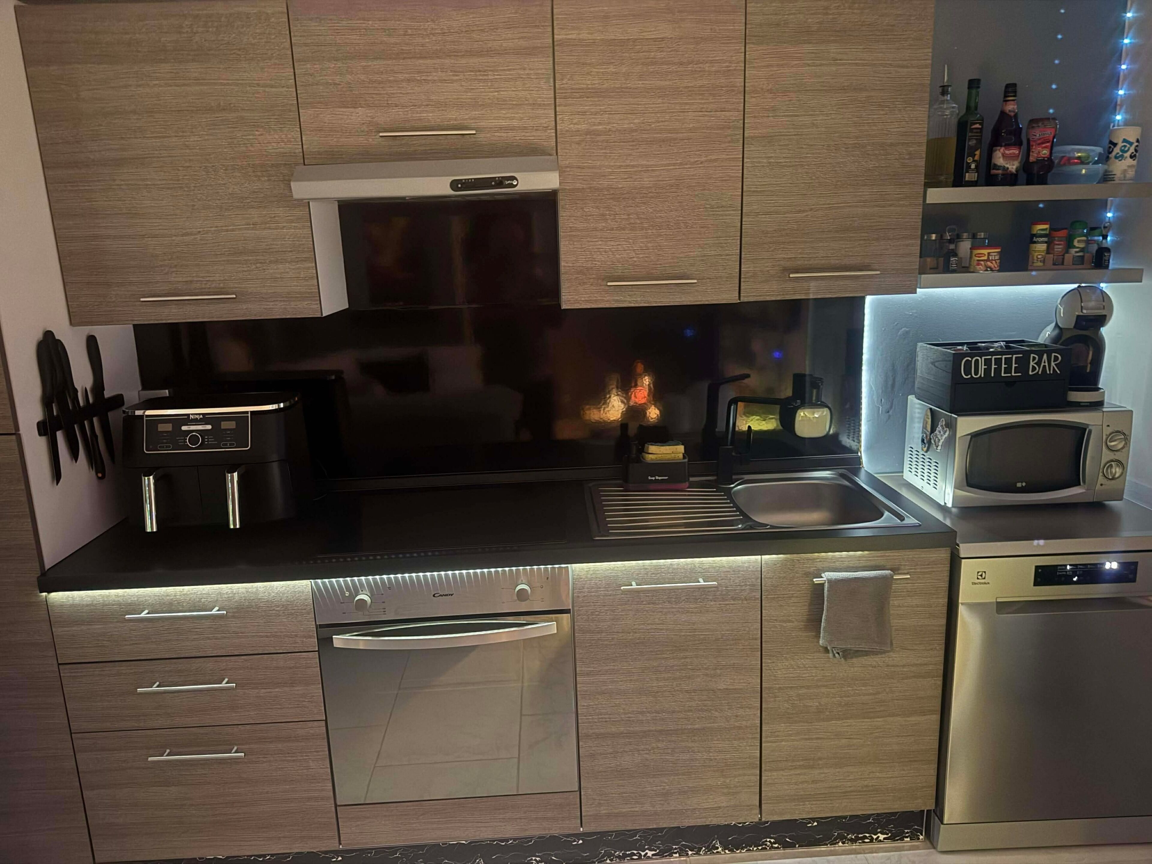 Une cuisine moderne dotée d’appareils électroménagers en acier inoxydable, de meubles en bois et d’un espace dédié à la préparation du café.