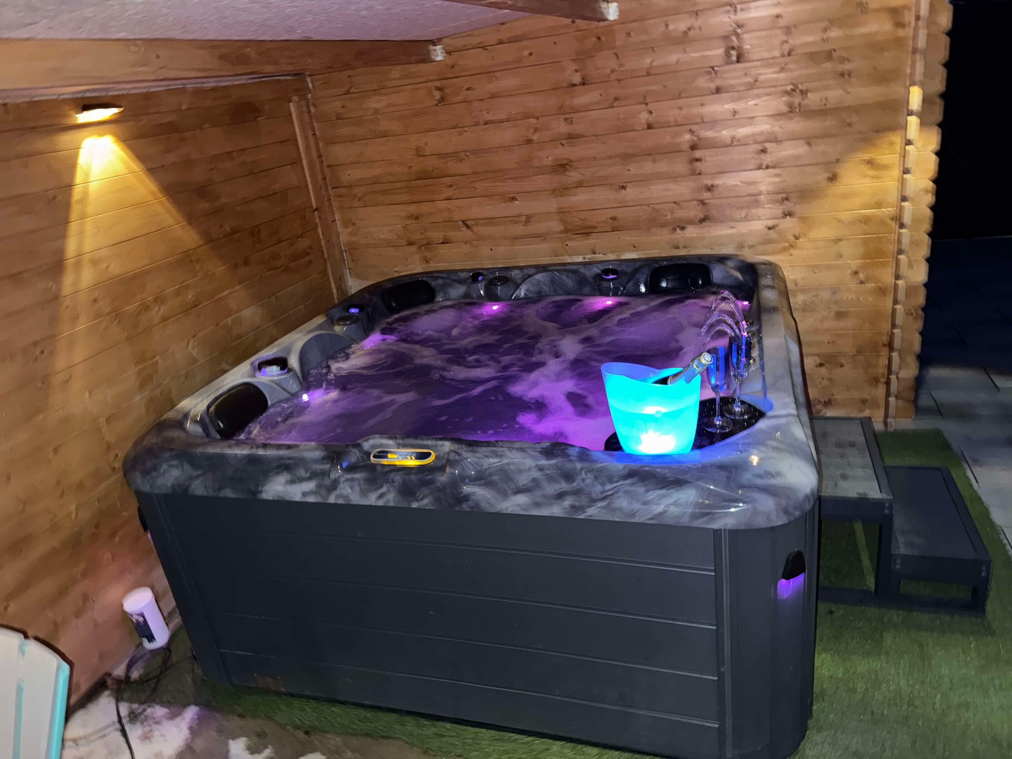 Ett bubbelbad med ett inre som liknar marmor och en inbyggd vattenfontän, omgivet av träväggar och ett litet trappsteg som leder ner till badet.