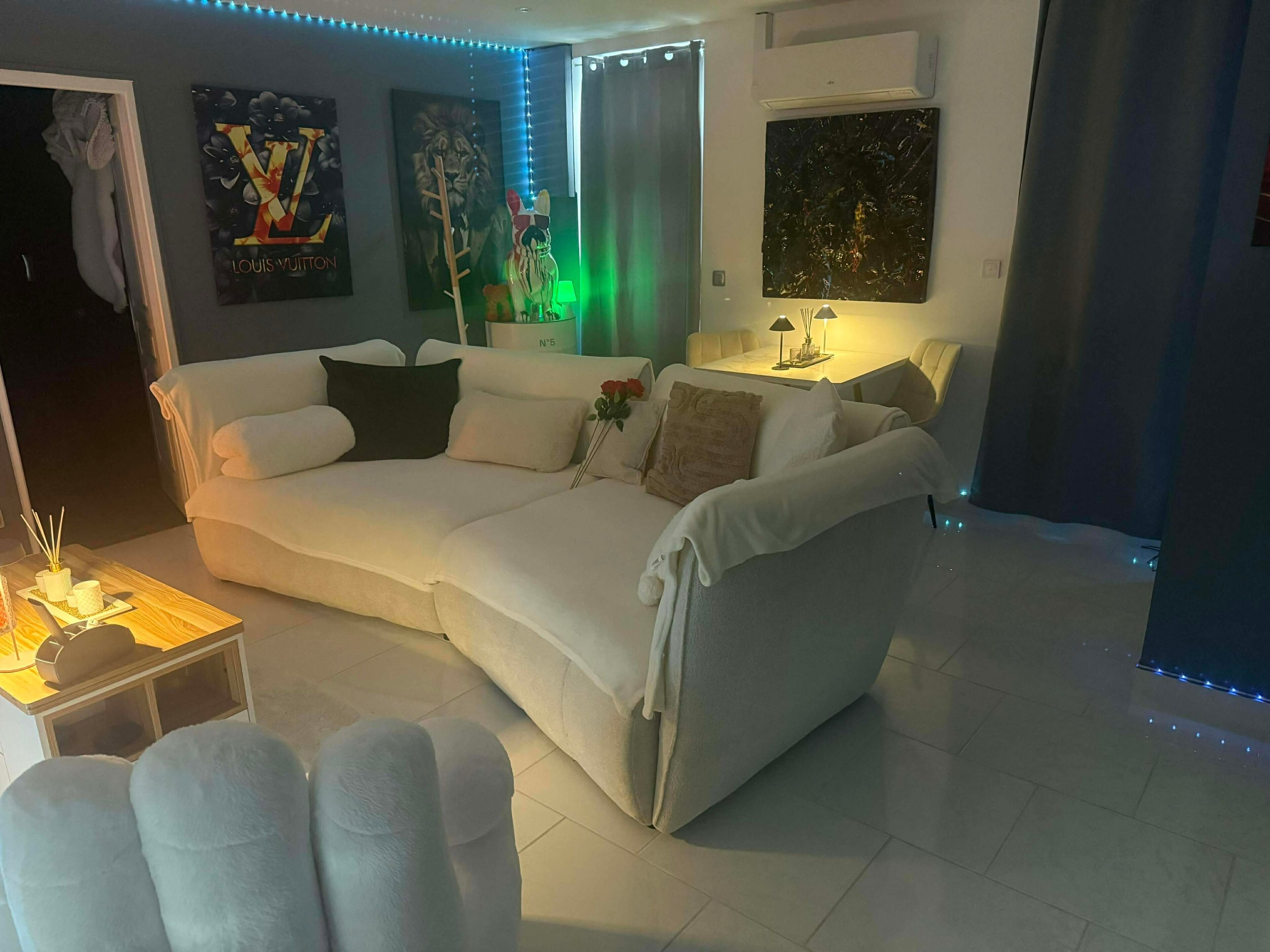 A modern living room with a white sofa, a small table with a lamp, and artwork on the walls.