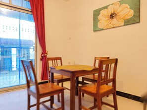 A dining area with a table and four chairs, a window with a view of buildings, and a flower painting on the wall. - Spacious Beachfront Apartment With Ocean Views in Uroa, Zanzibar (Uroa)