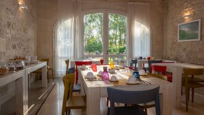 Un'area pranzo con parete in pietra rustica, ampie finestre ad arco e soffitto in legno.