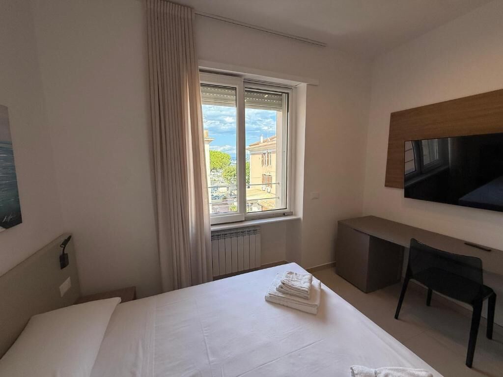 Une chambre d’hôtel avec un lit, un bureau, une chaise, une télévision et une fenêtre avec des rideaux.