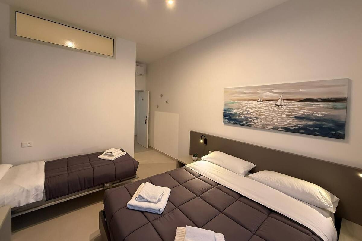 A modern hotel room with two beds, a painting of a sailboat, and a ceiling light fixture.
