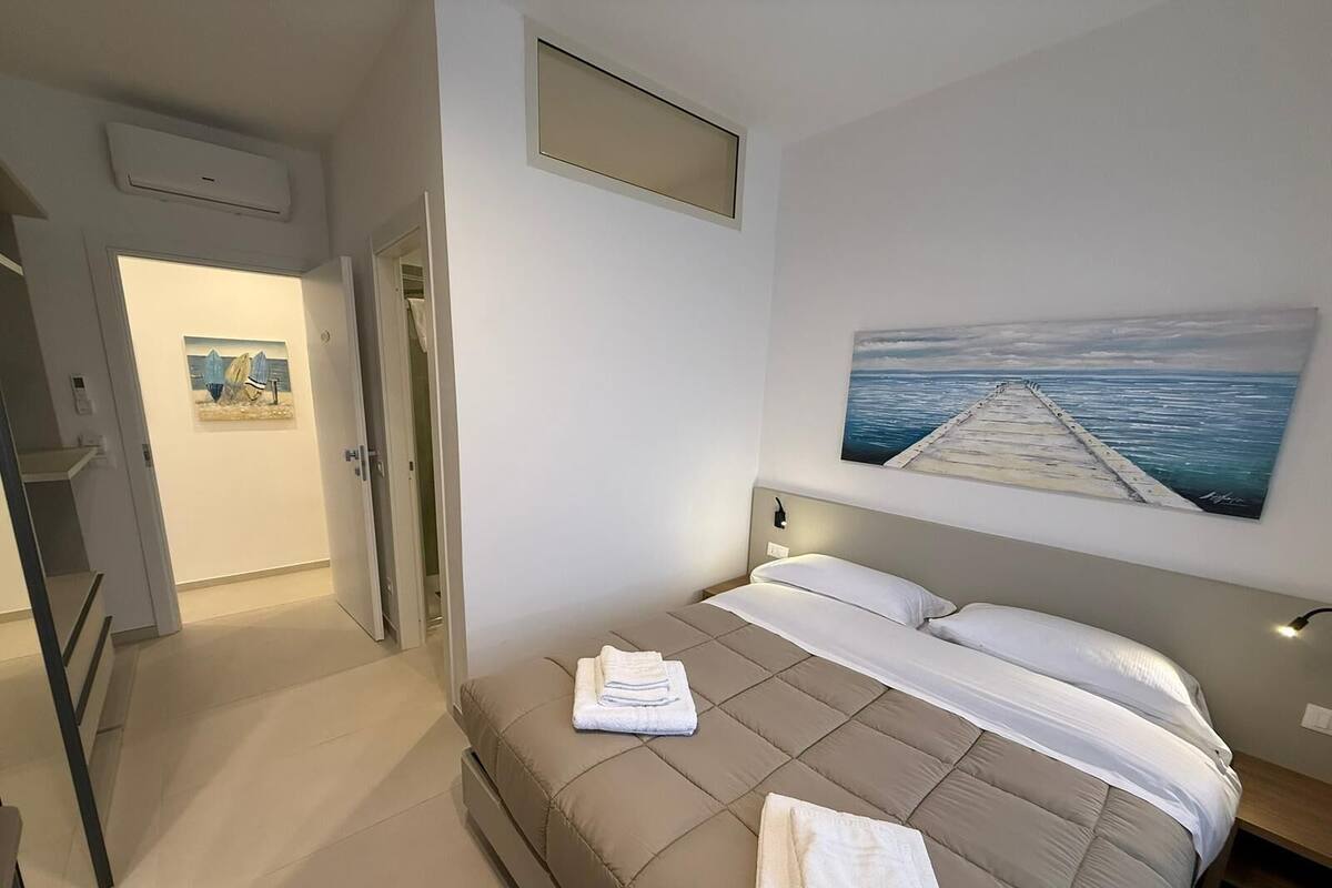 A bedroom with a bed, a painting of a pier, a door, and a staircase.