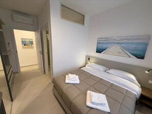 Un dormitori amb un llit, un quadre d'un moll, una porta i una escala.
